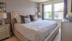 A bedroom with a large bed, a nightstand, a dresser, and a window with curtains. - Compass Bay 1610 (Kissimmee)