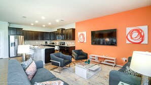 A modern living room with a gray sofa, two armchairs, a coffee table, and a kitchen area with dark cabinets and a refrigerator. - Windsor at Westside 8817 (Kissimmee)