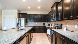 A modern kitchen with dark cabinetry, granite countertops, stainless steel appliances, and a tiled backsplash. - Windsor at Westside 8817 (Kissimmee)