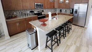 Une cuisine moderne avec des meubles en bois, des appareils en acier inoxydable, des plans de travail en granit et des tabourets de bar.