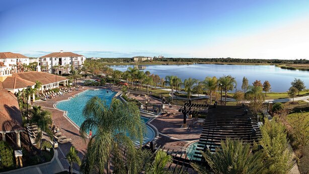 A resort with a large swimming pool, a tennis court, and a view of a lake.