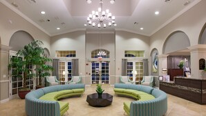 A spacious lobby with curved green sofas, a central coffee table, and a chandelier.