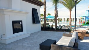 Une terrasse extérieure aménagée avec des meubles en osier, une cheminée et un espace piscine doté de parasols et de chaises longues.