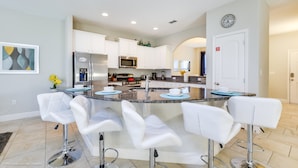 A modern kitchen with white cabinets, a central island with bar stools, stainless steel appliances, and a clock on the wall. - Solterra 4201 (Davenport)