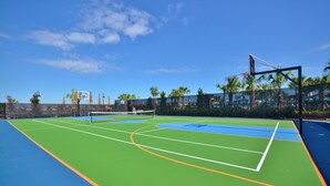 An outdoor tennis court with a net, surrounded by a fence and palm trees. - Windsor at Westside 8813 (Kissimmee)