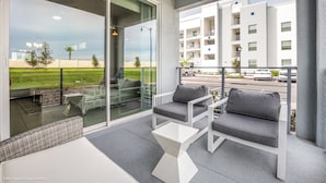 A balcony with a glass door, a white sofa, a small table, and a view of a building and street. - Storey Lake 4747-101 (Kissimmee)