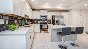 A modern kitchen with white cabinetry, stainless steel appliances, and a central island with bar stools. - Storey Lake 4747-101 (Kissimmee)