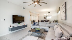 A modern living room with a flat-screen TV, a ceiling fan, and a dining area with chairs and a table. - Storey Lake 4747-101 (Kissimmee)