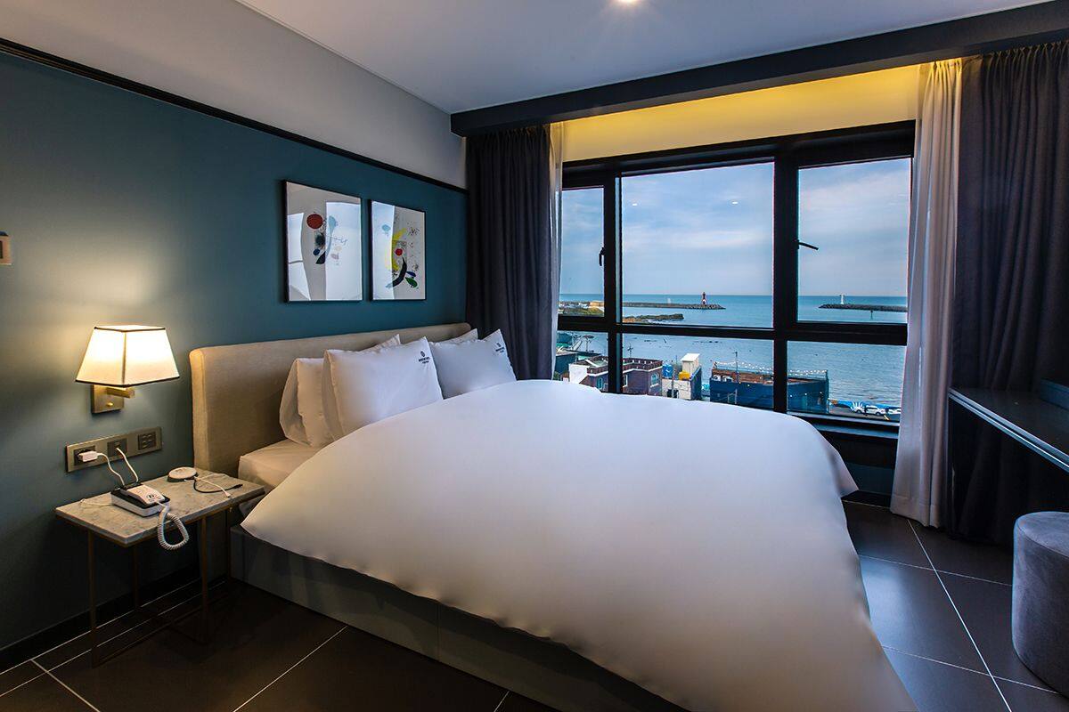 A hotel room with a large bed, a bedside table with a lamp, a phone, and artwork on the wall.