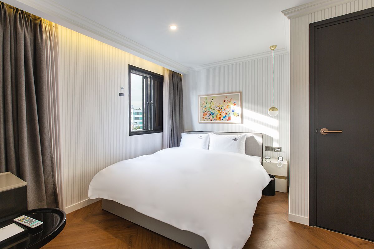 Een hotelkamer met een groot bed, een nachtkastje met een lamp, een raam met gordijnen en een deur.