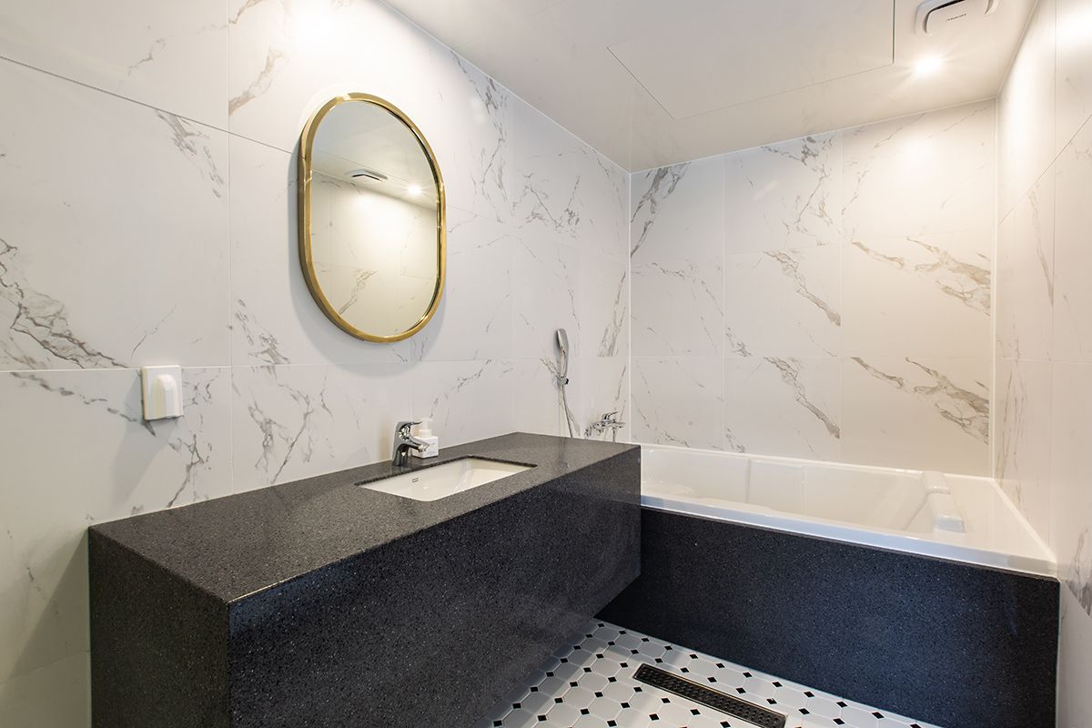 Un bany modern amb paret de marbre, un lavabo de granat negre, un mirall amb marc daurat i una banyera blanca.