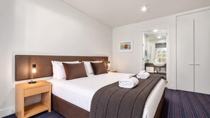 A hotel room with a bed, bedside table, lamp, towels, a bathroom with a sink, and a mirror.