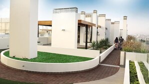 A rooftop terrace with a circular grassy area, white pillars, and a clear view of the city skyline.