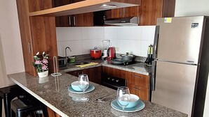 A modern kitchen with a granite countertop, stainless steel appliances, wooden cabinets, and black bar stools.