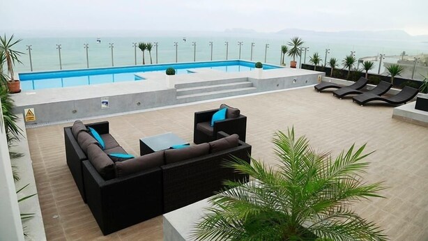 A rooftop pool area with a view of the sea, lounge chairs, and a sofa.