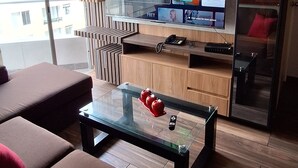 A modern living room with a large flat-screen TV mounted on a wooden wall, a glass coffee table with red decorative items, and brown sofas with red cushions.