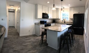 Kitchen with a large island, white cabinetry, and a black refrigerator, adjacent to a hallway leading to the Beach House.