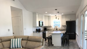 A modern kitchen with white cabinets, a black refrigerator, and a bar stool.