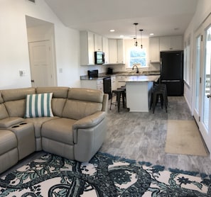 Relax in this cozy living space with a kitchenette, featuring a sofa, patterned rug, and small island with stools.