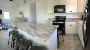 A modern kitchen with white cabinets, a marble countertop, and a black stove.