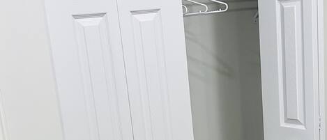 A white closet with a hanging rod and a rolled-up carpet.