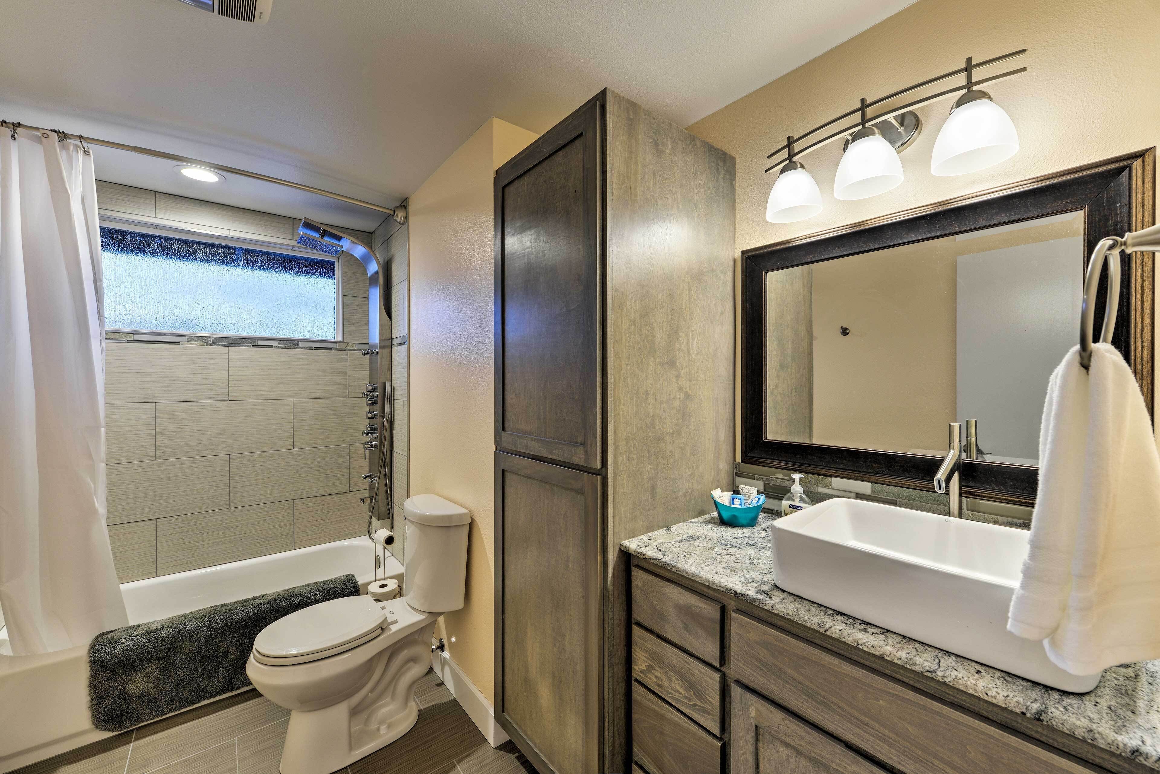 A bathroom with a bathtub, toilet, vanity with a sink, and a large mirror.