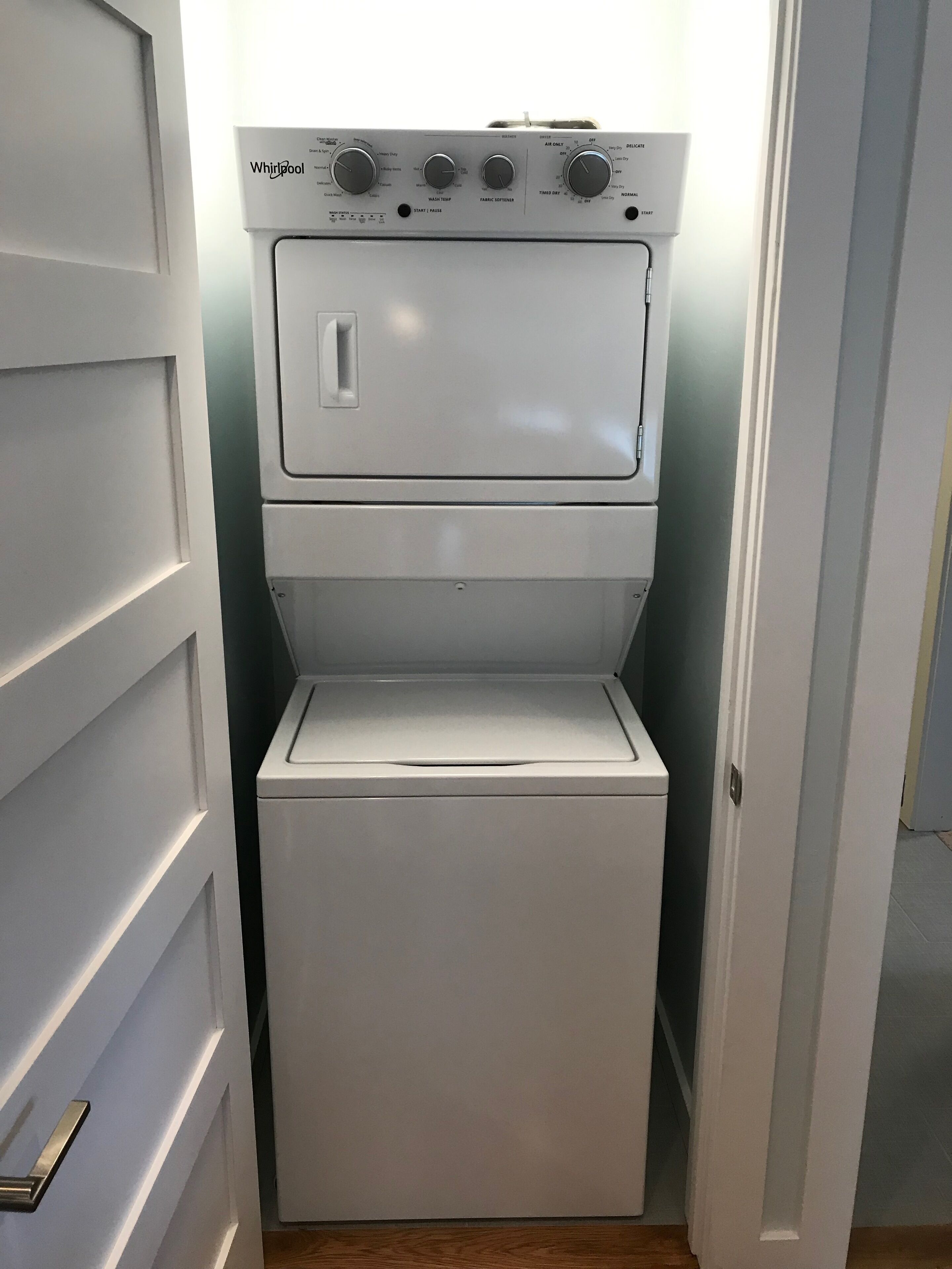 Una unidad compacta de lavadora y secadora Whirlpool blanca en un pasillo estrecho.