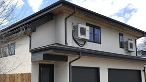 A two-story building with a garage and two air conditioning units mounted on the exterior wall.
