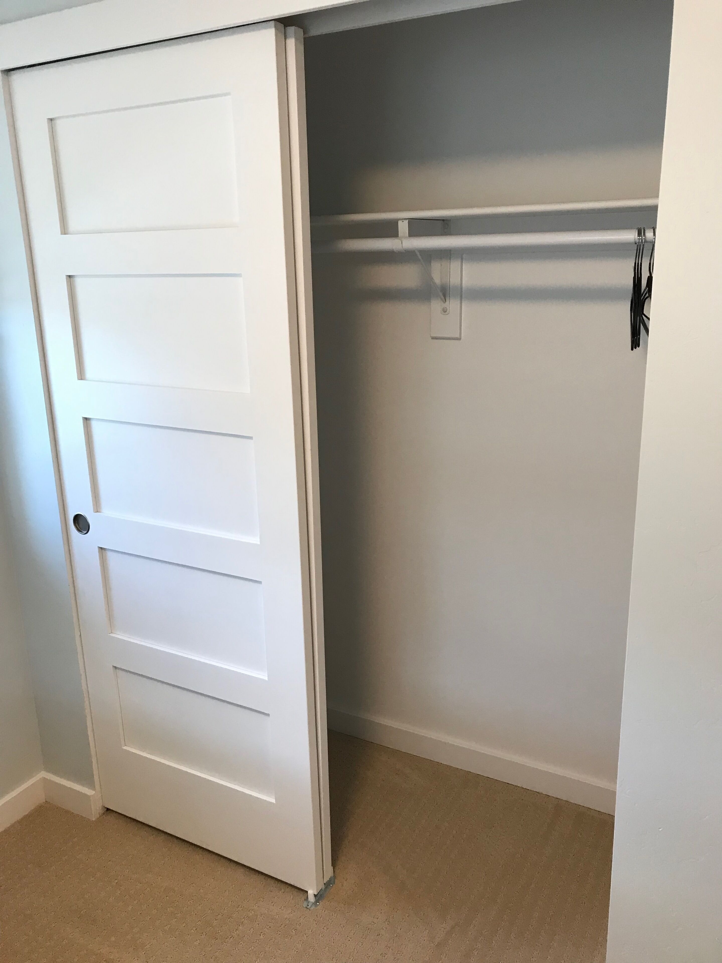 A closed white door with a handle, a closet with a rod, and a light switch on the wall.