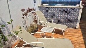 En terrasse med to liggestole og et lille bord, omgivet af plantede planter og en flisevæg.