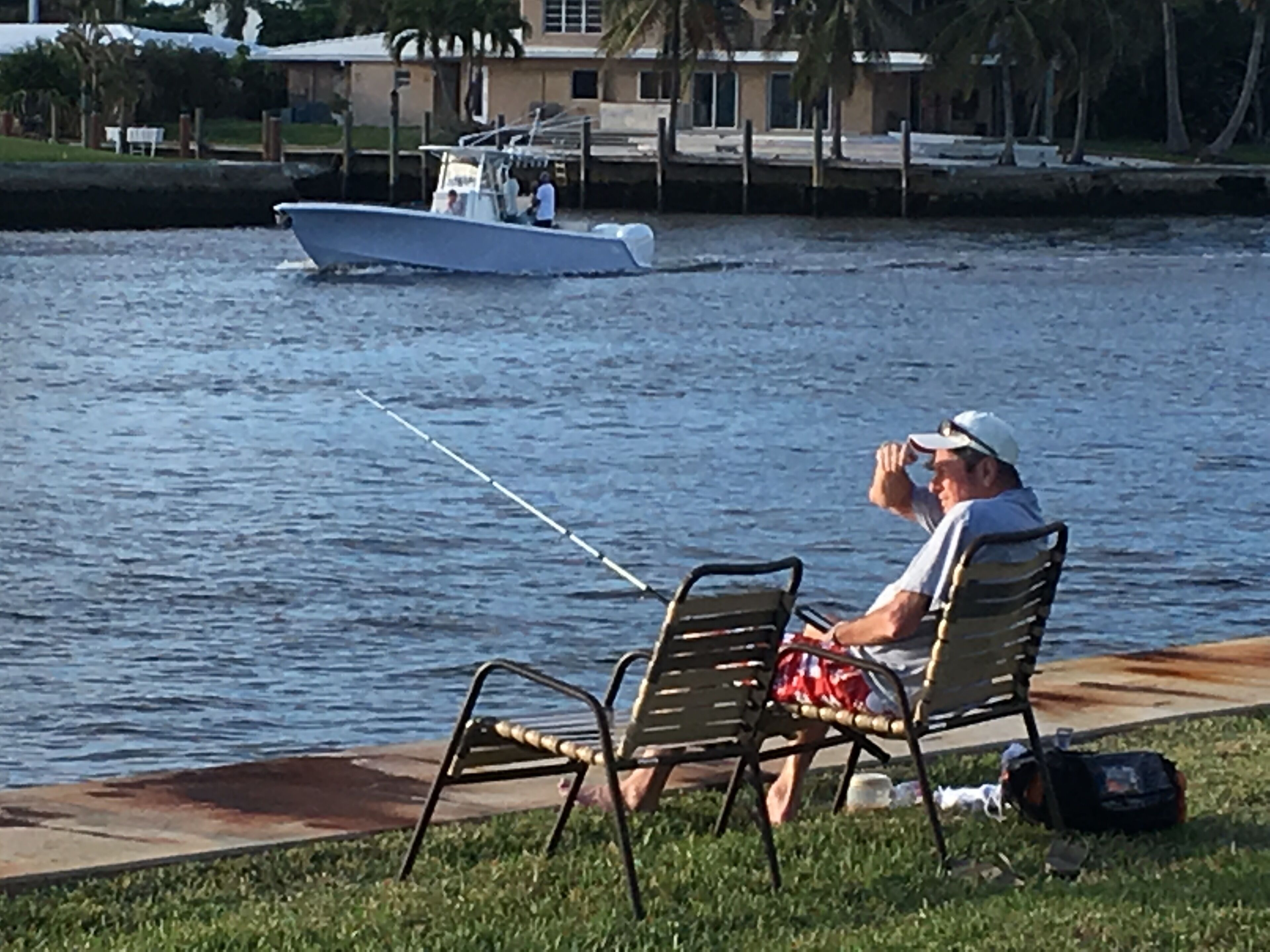 Un hombre pesca en un cuerpo de agua tranquilo, con un bote al fondo.