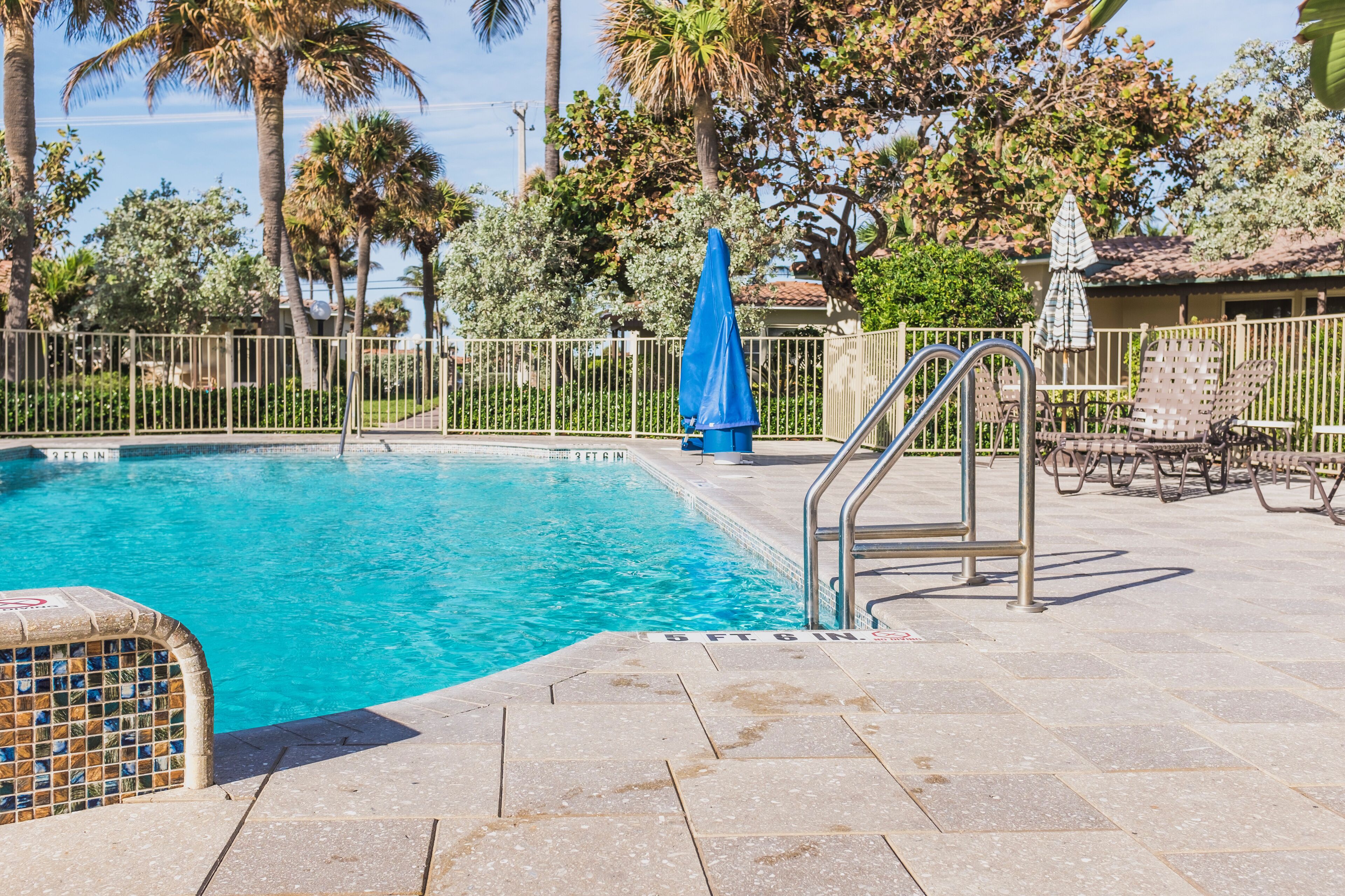 A swimming pool with a tiled edge, a metal ladder, and a blue umbrella.