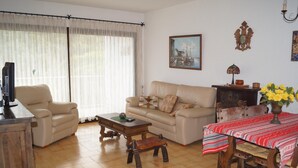 Un saló amb un sofà, una butaca, una taula de centre i una taula de menjador amb un mantell vermell.