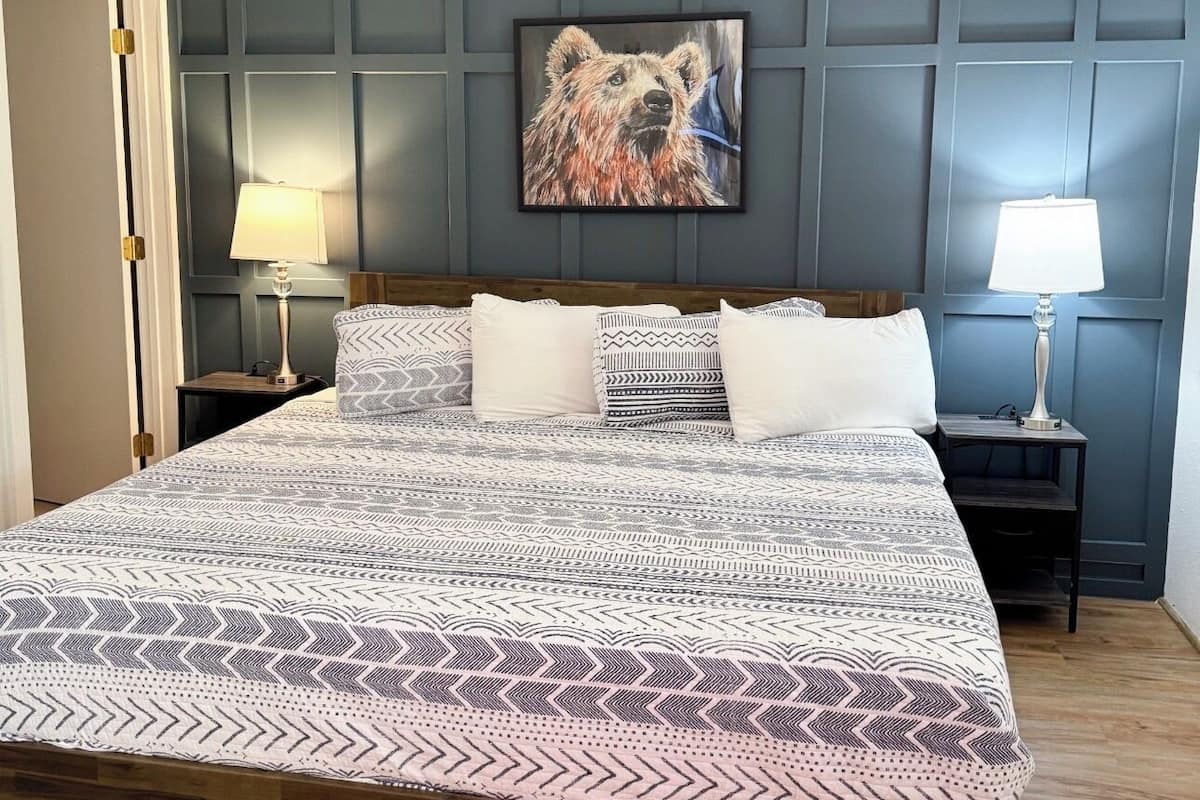 Ein Schlafzimmer mit einem großen Bett, zwei Nachttischen, einem Wandbild und einer Tür.