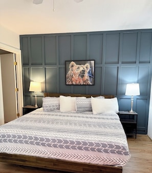 A bedroom with a large bed, two bedside tables, a wall-mounted painting, and a door.