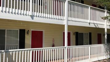 A two-story building with a white balcony railing, red doors, and a clear blue sky in the background.