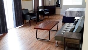 A room with a wooden floor, a sofa, a table, and a ceiling fan. - The Caden Hotel (Vernonia)