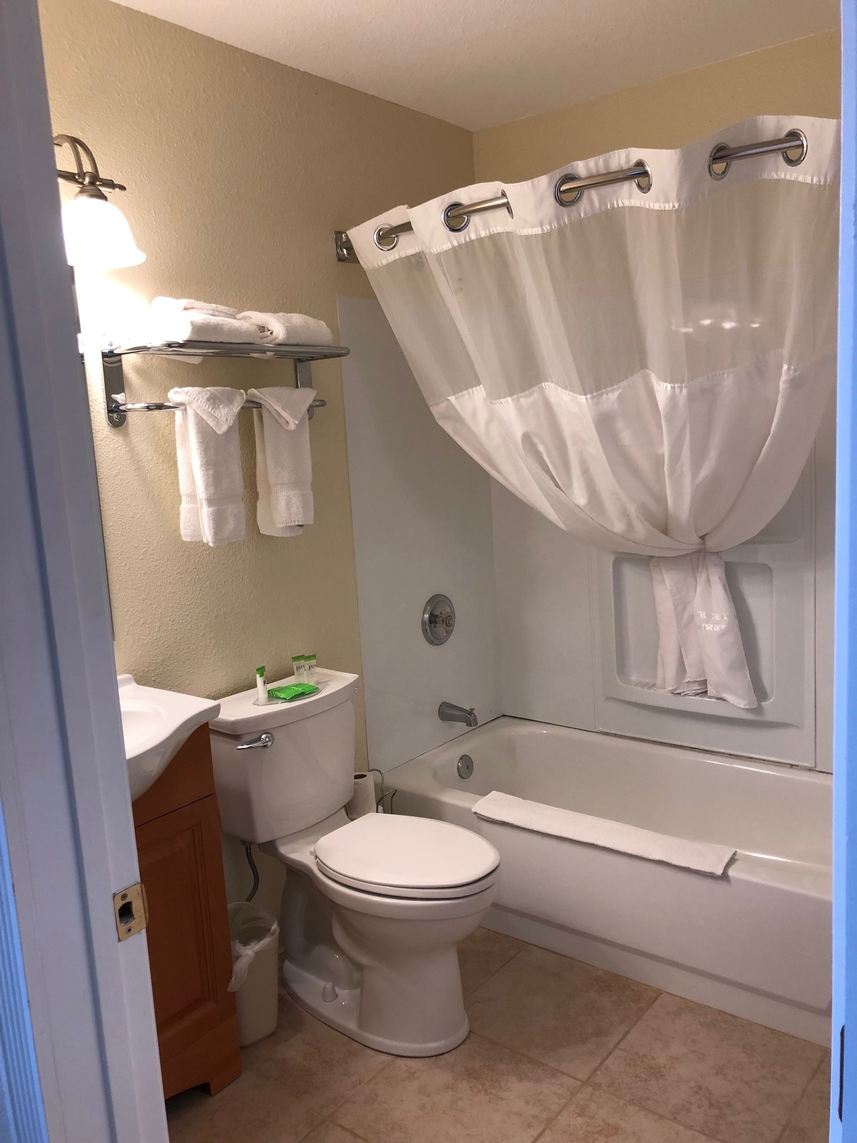 Een badkamer met toilet, wastafel en bad. Handdoeken hangen aan de muur en er is een douchegordijn.