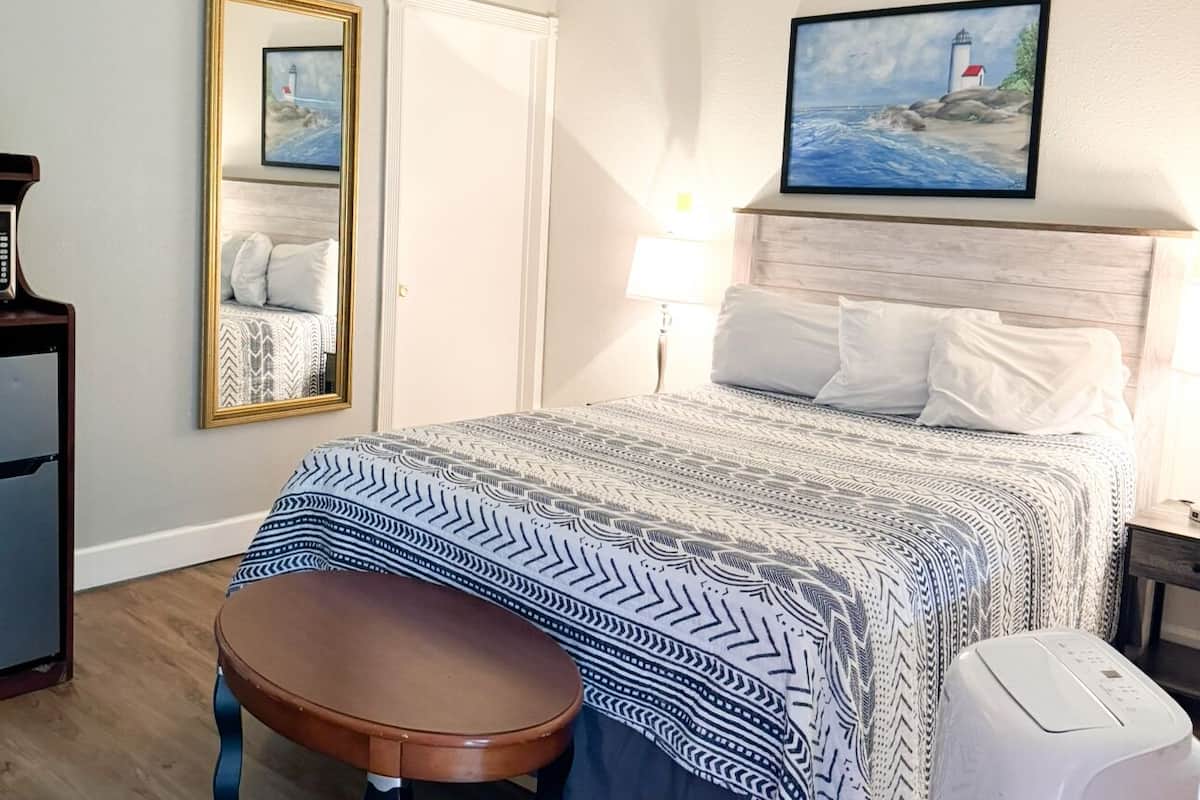 Ein Schlafzimmer mit einem Bett, einem runden Tisch, einem Spiegel und einem Gemälde eines Leuchtturms.