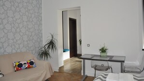 Een woonkamer met een bank, een salontafel, een bijzettafeltje met een plant, en een deur naar een andere kamer.