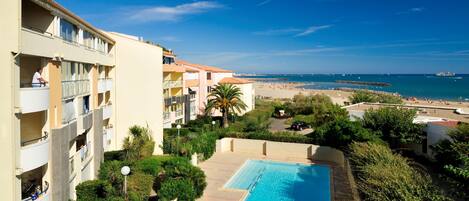 A hotel with a swimming pool, balconies, and a view of the beach.