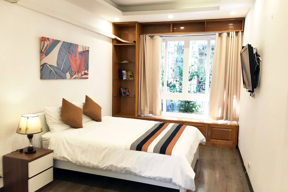 A neatly arranged bedroom with a bed, bedside table, and a window with curtains.