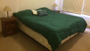 Ein Schlafzimmer mit grüner Bettdecke, zwei Nachttischlampen, einem Nachttisch und einem Fenster mit Vorhängen.