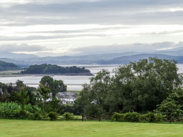 A coastal landscape with a grassy foreground, a body of water, and distant hills.