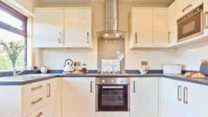 Una cocina moderna con armarios blancos, una campana extractora de acero inoxidable, horno empotrado y ventana con vistas a zonas verdes.