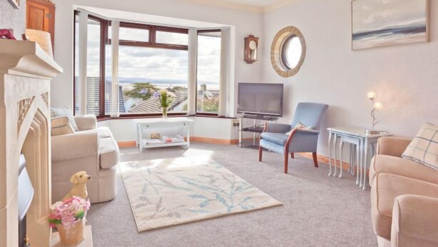 Una sala de estar con chimenea, televisor, sofá, mesa de centro y vistas a la ciudad a través de amplios ventanales.