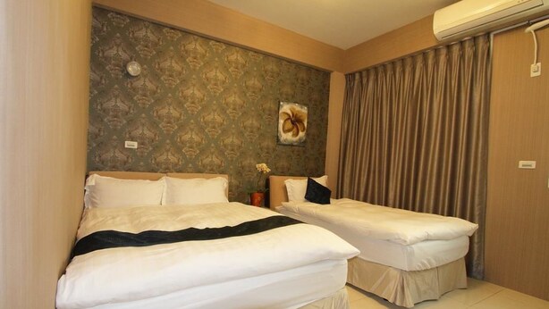 A hotel room with two beds, a patterned wallpaper, a wall-mounted air conditioner, and a curtain. - Hilarity B&B (Hualien City)