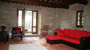 Une pièce chaleureuse avec un mur en pierre, un canapé rouge, un fauteuil à bascule en bois et un lit blanc.