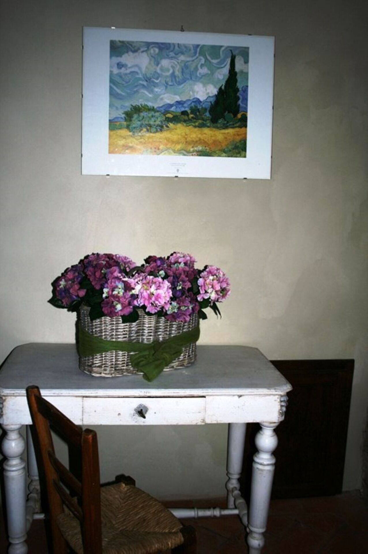 A table with a basket of flowers and a framed painting above it.