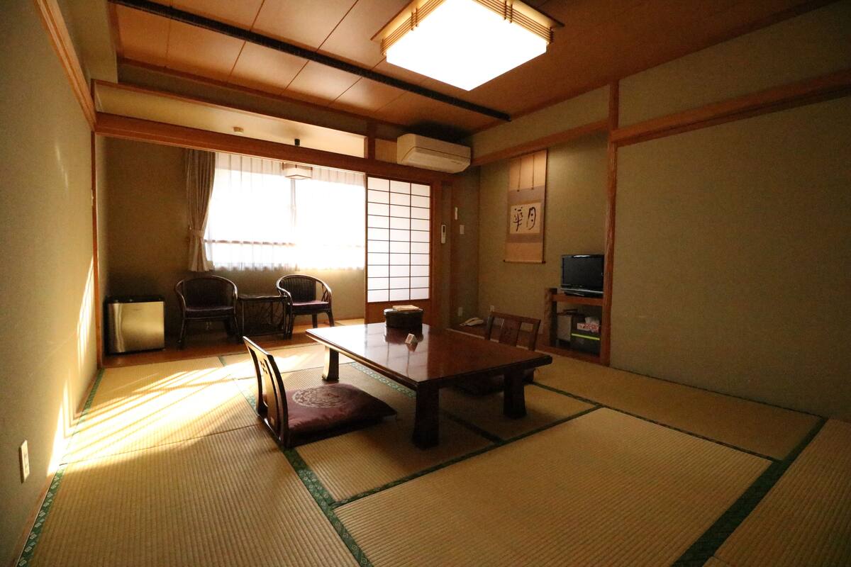 A traditional Japanese room with tatami flooring, a low table, chairs, a television, and sliding doors.